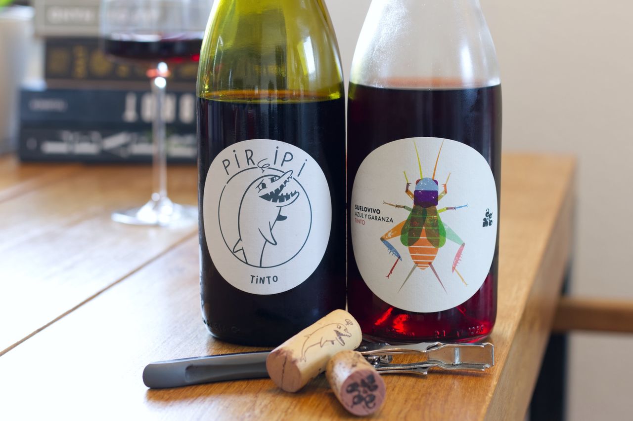 Two bottles of wine from the Azul y Garanza winery sit on a wooden table. In the background you can see a wine glass and a stack of books. The corks lie in front of the bottles, still on the waiter's knife.