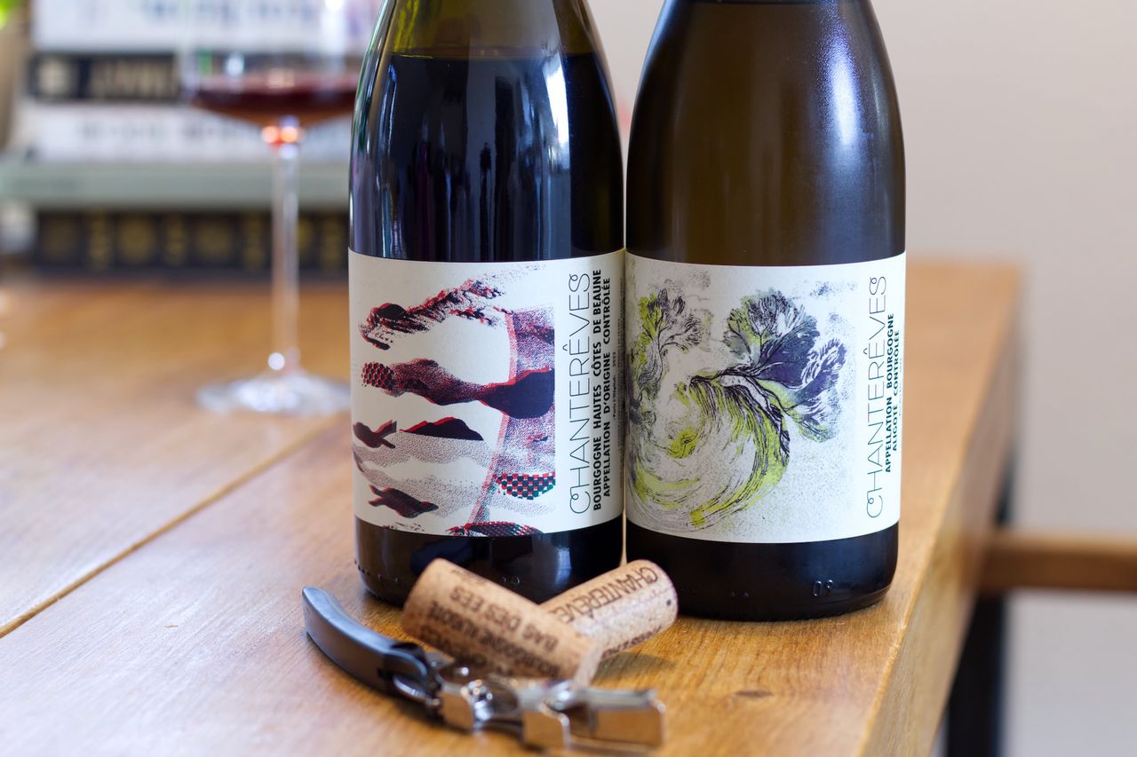 Two bottles of wine from the Chanterêves winery stand on a wooden table. In the background you can see a wine glass and a stack of books. In front of the bottles the corks lie on the waiter's corkscrew.